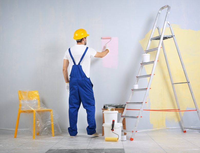 Young worker painting wall in room